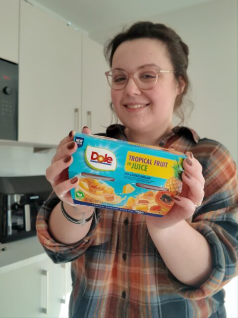 AD PR Taste-testing some Dole fruit pots that landed on my doorstep - the perfect little snack for when your having a chronic illness day and need to reach for something sweet. 🌞✨ Each pot is excellent source of vitamin C with no added sugar - I'm going to start keeping some of these in my hospital bag, as they are stoma-friendly for me, last a long time and don't need to be refrigerated.Thank you @dolesunshineukVD:
Image 1: A white woman with brown wavy hair, wearing a shirt and glasses whilst smiling. She is holding a pack of fruit juice pots from Dole in a kitchen environment.
Image 2: A white woman with brown wavy hair, wearing a shirt and glasses whilst smiling. She is holding a pack of fruit juice pots from Dole, along with an open pot and spoon.
Image 3: A close-up view of a fruit pot and spoon, ready to go into a hospital bag.
