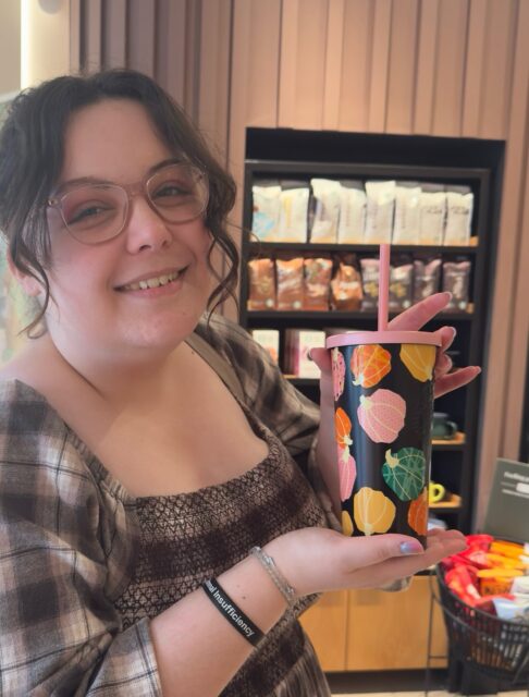 Spotted pumpkin cups at @starbucksuk and squealed out loud! My season is coming 🍂Ready to claim rightful spot on the PSL lovers top 5 as is annual tradition. 👀VD: A white woman, with brown wavy hair smiling, holding a black cup with multicolour pastel pumpkins on it against a black background. Photos two is a close up of these.