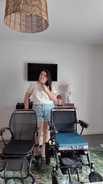Episode 5 of The Wheel Deal: Everyday chair or just for occasions?VD: A white woman with brown hair, stood talking to you with two black powered wheelchairs nearby.