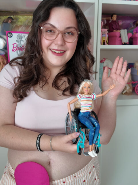 The countdown to World Stoma Day on the 3rd October is on!
Me and Barbie are getting ready...Spy my stunning stoma cover from @adaptedtrendsclothingukVD: A white woman with brown hair, wearing a pink top and pink stripe trousers. She has a stoma bag on show, with a pink cover on. She is holding a Barbie in a wheelchair, with Barbies in the background on shelves.