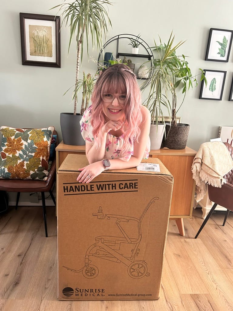 Lady with pink hair posting with Q50R wheelchair box