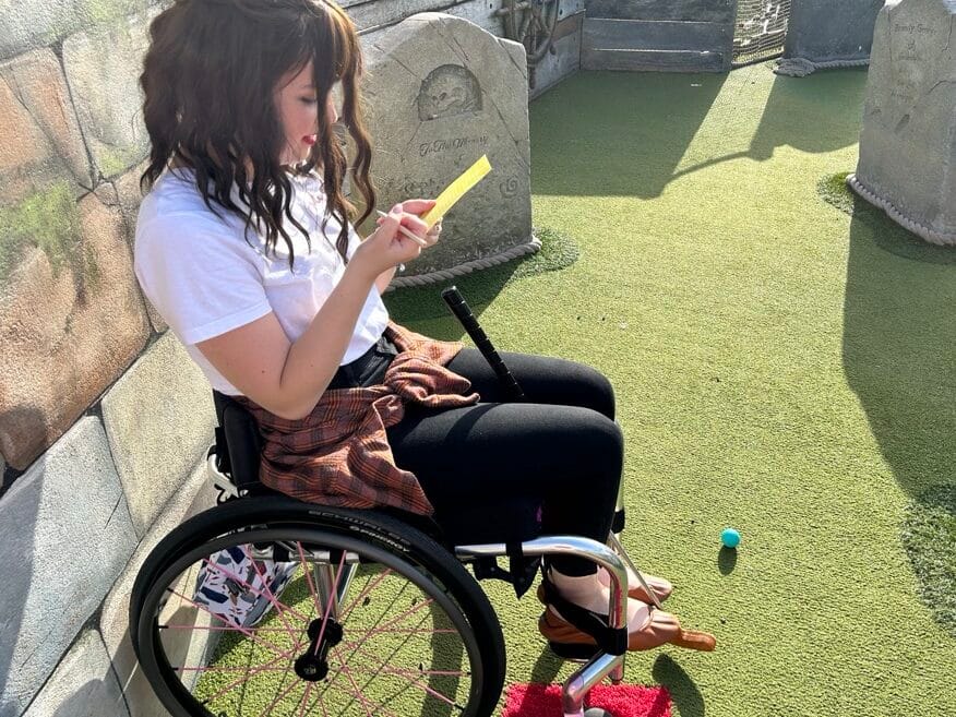 Woman with brown hair, sat using phone in manual wheelchair